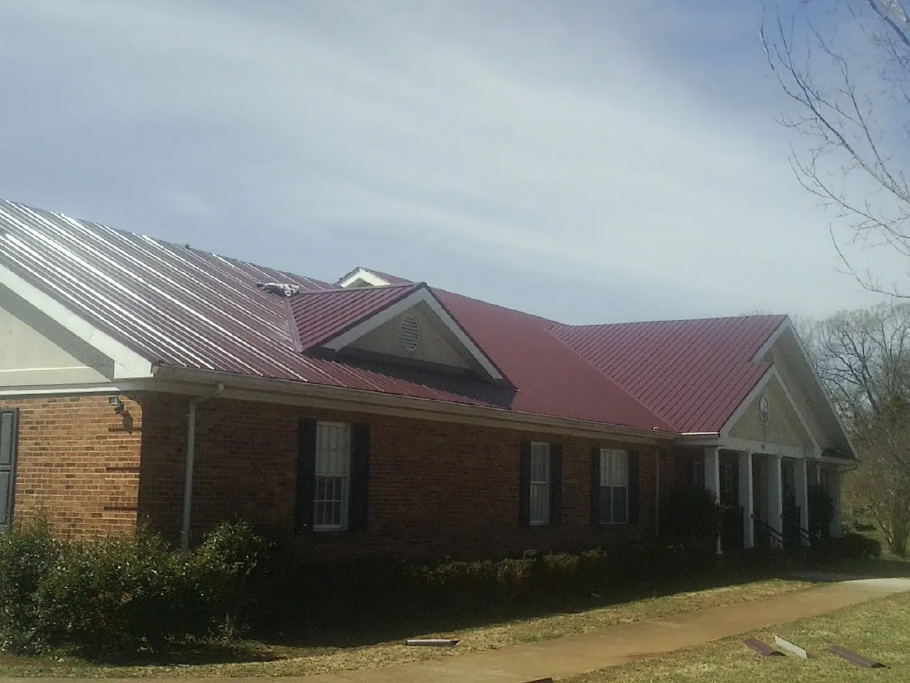 Red metal roof with gabled entries on a long brick building, from a Hail Damage Roof Repair job in Mount Ulla