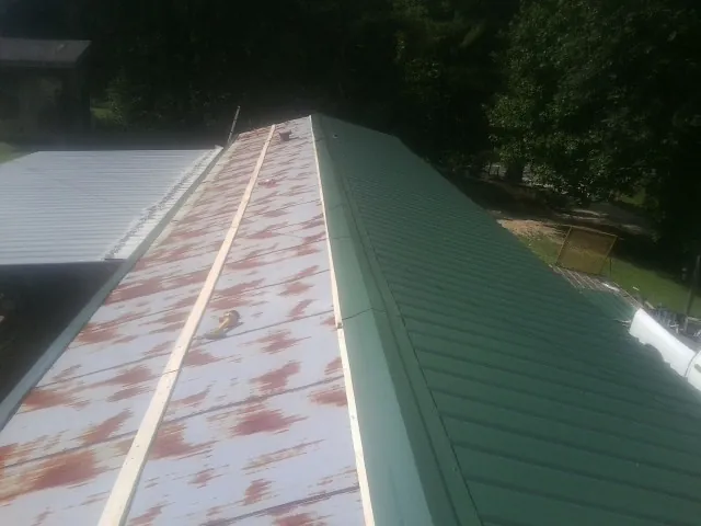 Old rusted panels beside newly installed green metal roofing — Wind Damage Roof Repair by Roofing Brothers in Mount Ulla