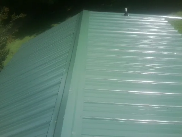New green metal panels meeting at the ridge of a roof — Flat Roof Repair work by our crew in Mount Ulla